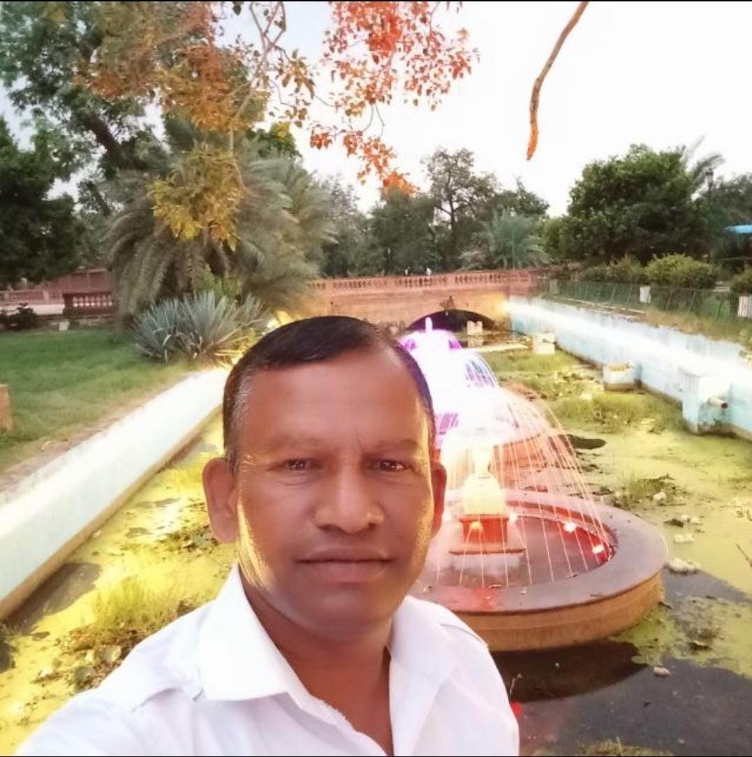 a man taking a selfie outdoors, with a tree, grass, and the sky in the background