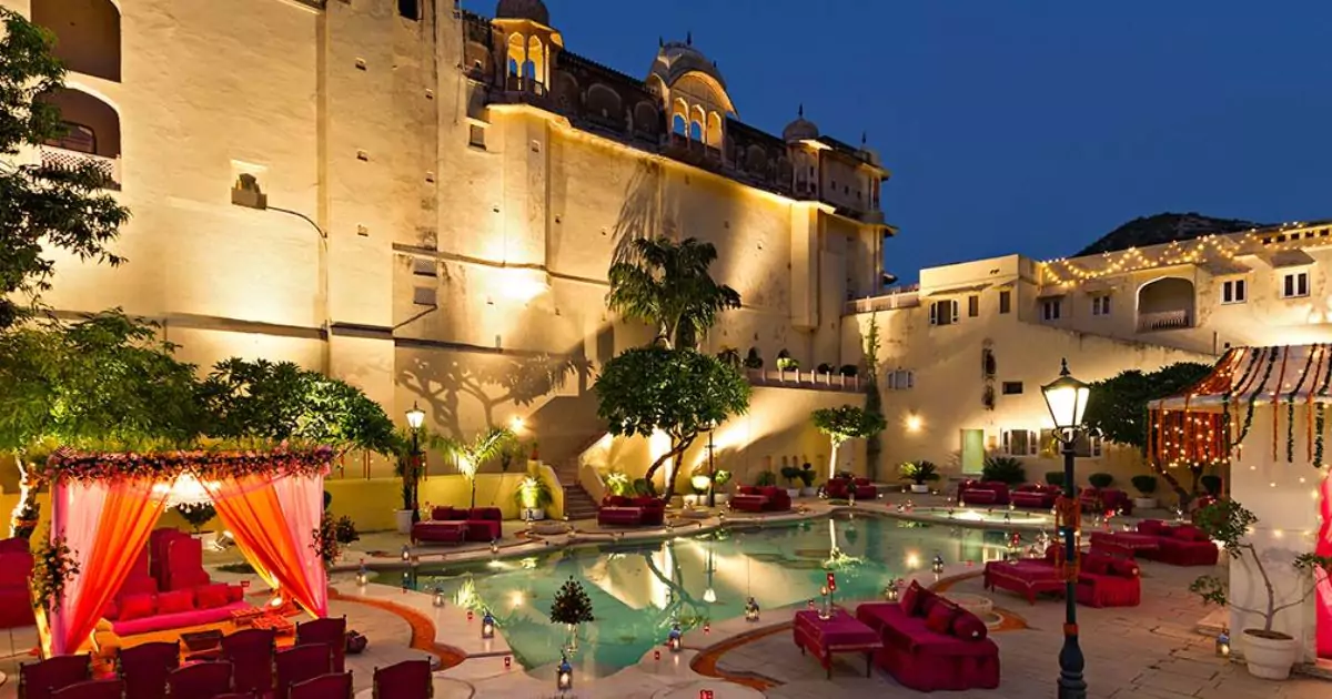 A luxurious heritage resort in Jaipur featuring a beautifully lit pool, ornate architecture 