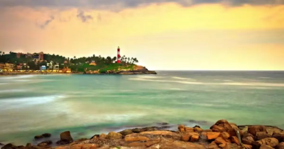 Kovalam beach at sunset with lighthouse and rocky shore. 